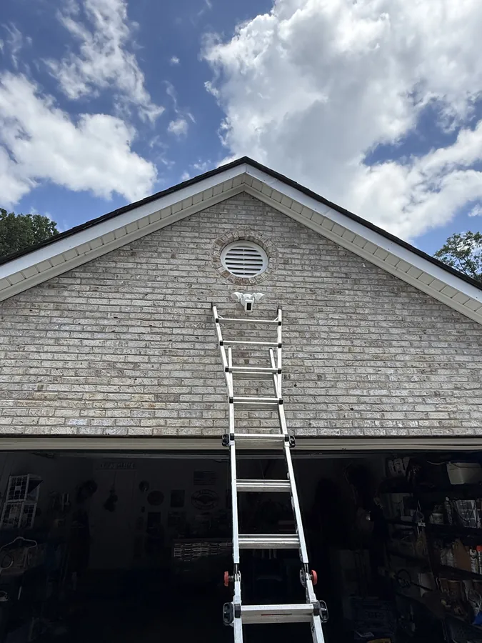 Floodlight camera being installed high on a brick gable, ladder up against the house
